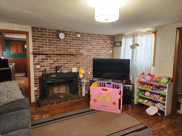 recreation room featuring a textured ceiling, a baseboard heating unit, wood finished floors, and a brick fireplace