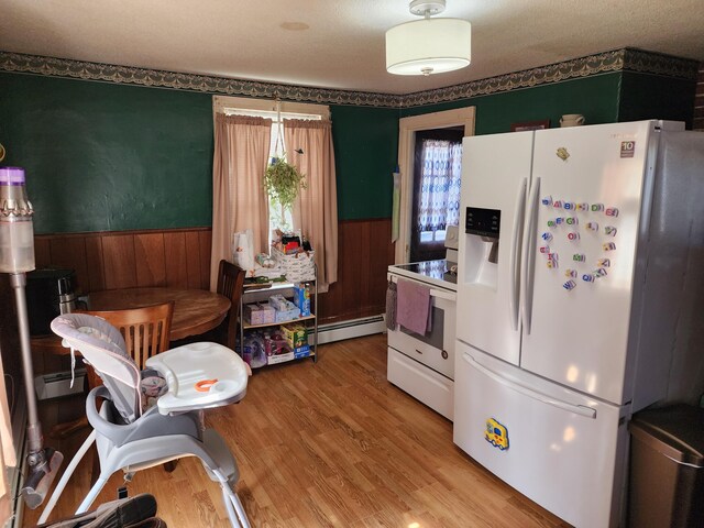 kitchen with wainscoting, baseboard heating, white appliances, and a healthy amount of sunlight