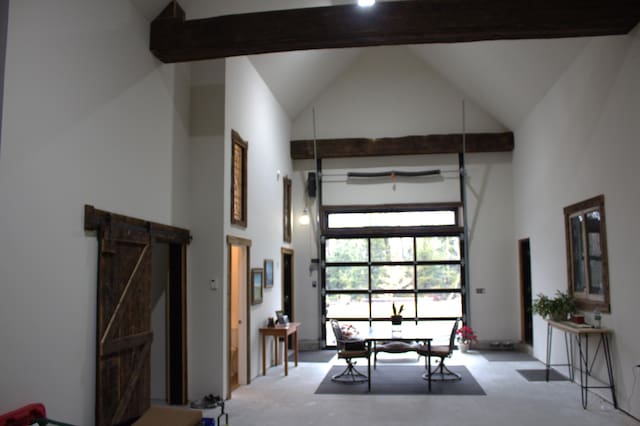 carpeted dining area with a barn door, high vaulted ceiling, and beamed ceiling
