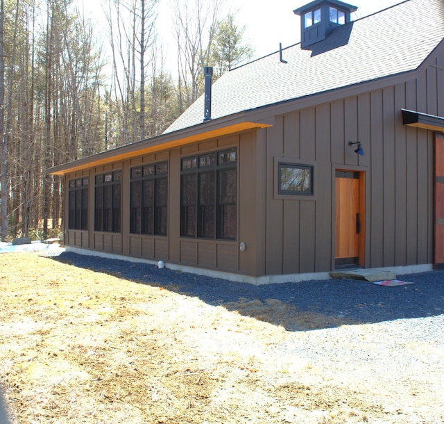back of house featuring board and batten siding, a shingled roof, and a sunroom