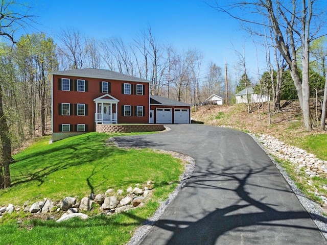 colonial-style house featuring an attached garage, a front yard, and aphalt driveway