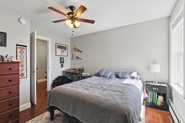 bedroom with ceiling fan, wood finished floors, baseboards, and a baseboard heating unit