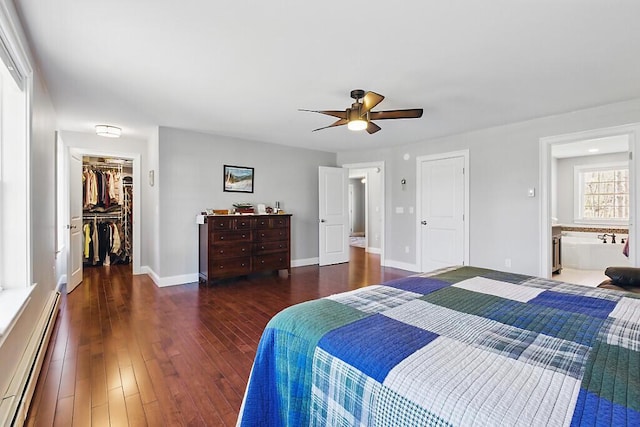 bedroom with a closet, wood finished floors, a baseboard radiator, ceiling fan, and a walk in closet