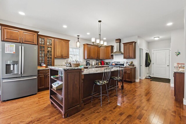 kitchen featuring a center island, open shelves, wall chimney exhaust hood, appliances with stainless steel finishes, and hardwood / wood-style flooring