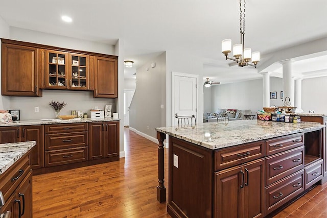 kitchen featuring pendant lighting, glass insert cabinets, dark wood-style floors, and ornate columns