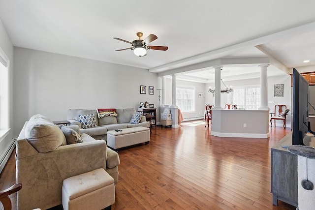living room featuring wood finished floors, ceiling fan with notable chandelier, ornate columns, baseboards, and a baseboard heating unit
