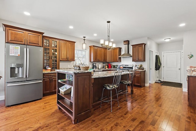 kitchen featuring a center island, open shelves, wall chimney exhaust hood, stainless steel refrigerator with ice dispenser, and dark wood-style floors