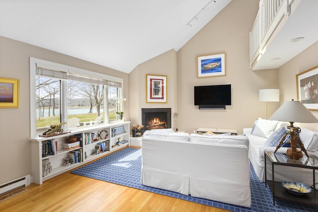 53 Jameson Point Rd Unit 24, Rockland, ME 04841 - living room with wood finished floors, track lighting, vaulted ceiling, a baseboard radiator, and a lit fireplace