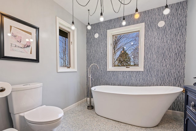 full bathroom featuring baseboards, speckled floor, a freestanding bath, and toilet