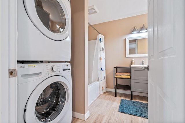 washroom featuring laundry area, stacked washing maching and dryer, baseboards, a sink, and light wood finished floors