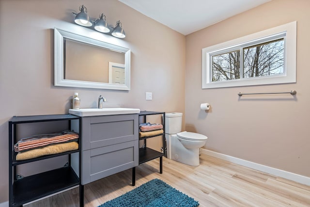 half bath featuring baseboards, vanity, toilet, and wood finished floors