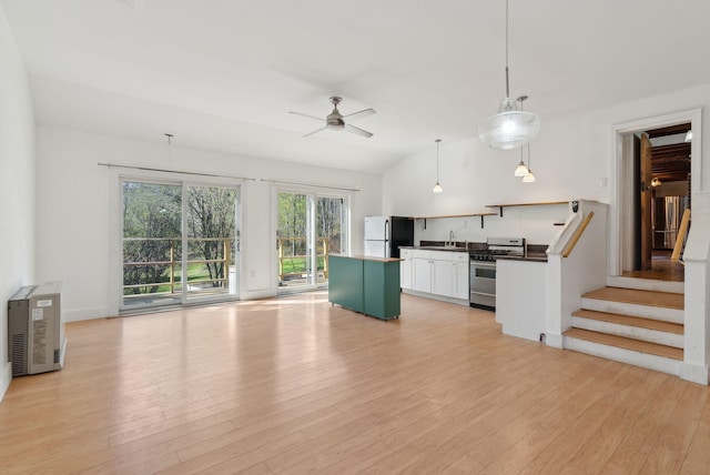 kitchen featuring freestanding refrigerator, dark countertops, ceiling fan, stainless steel gas range oven, and light wood-style flooring