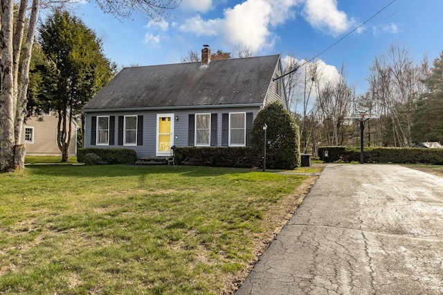 cape cod-style house with roof with shingles, driveway, a chimney, and a front yard