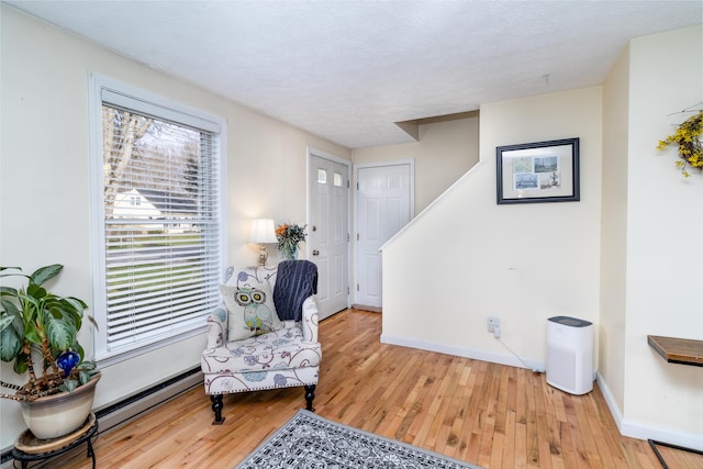 living area with baseboards, a baseboard heating unit, light wood-type flooring, and a textured ceiling
