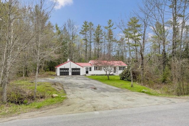 view of front of house with an attached garage, asphalt driveway, a front lawn, metal roof, and a forest view