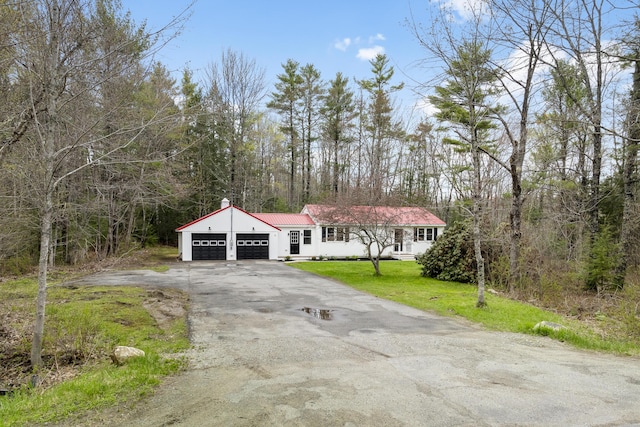 view of front of house featuring a garage, asphalt driveway, a front lawn, metal roof, and a wooded view