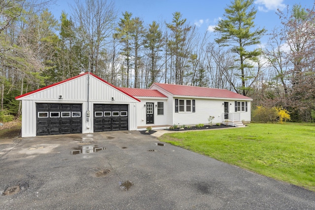 view of front of property featuring board and batten siding, an attached garage, asphalt driveway, metal roof, and a front lawn