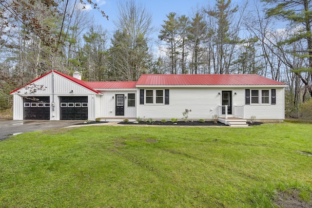 view of front of property featuring asphalt driveway, an attached garage, a chimney, a front lawn, and metal roof