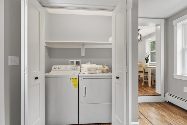 clothes washing area featuring washing machine and dryer, a baseboard radiator, wood finished floors, and a chandelier