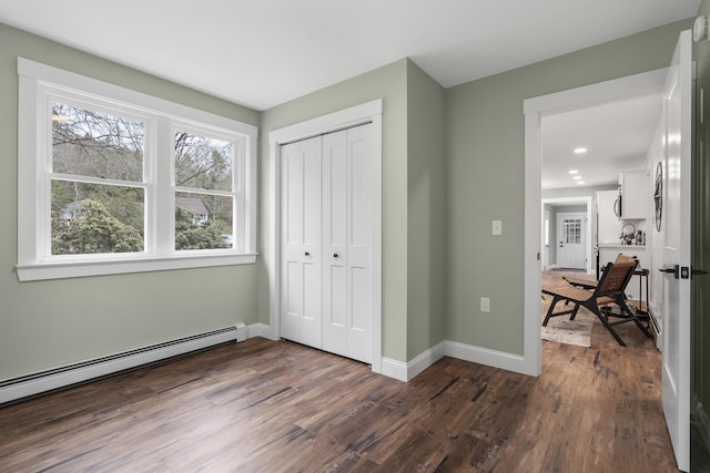 unfurnished bedroom with baseboard heating, dark wood-style flooring, baseboards, and a closet