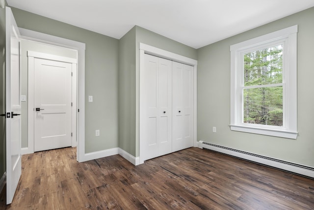 unfurnished bedroom featuring baseboard heating, dark wood finished floors, a closet, and baseboards