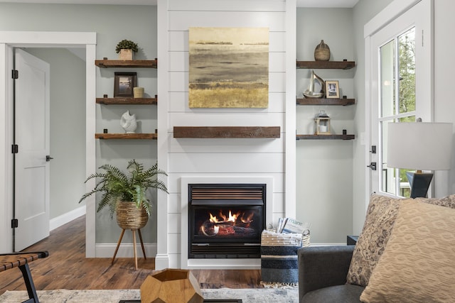 living room featuring wood finished floors, baseboards, and a lit fireplace