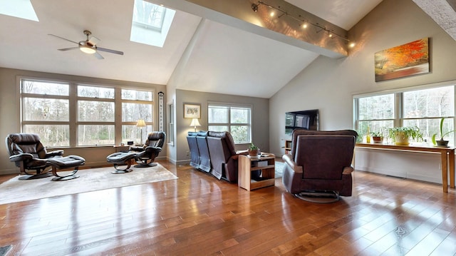 living area featuring a ceiling fan, a skylight, rail lighting, wood finished floors, and high vaulted ceiling