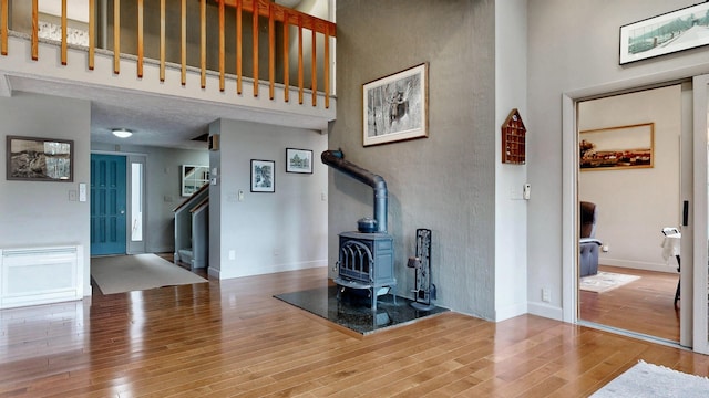 unfurnished living room with a wood stove, baseboards, wood finished floors, a towering ceiling, and stairway