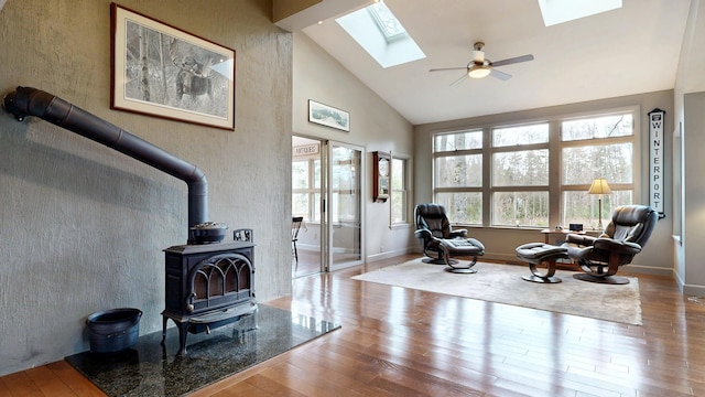 sitting room with a skylight, wood finished floors, a wood stove, and high vaulted ceiling