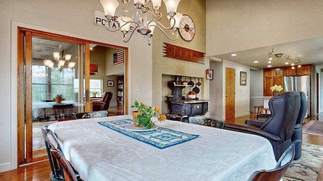 dining space featuring an inviting chandelier, a wood stove, light wood-type flooring, and a towering ceiling