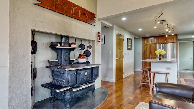 kitchen with freestanding refrigerator, wood finished floors, a kitchen breakfast bar, recessed lighting, and brown cabinets