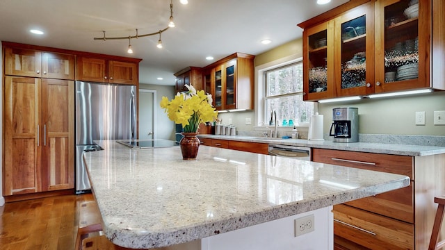 kitchen with brown cabinetry, a kitchen island, appliances with stainless steel finishes, light stone countertops, and a sink
