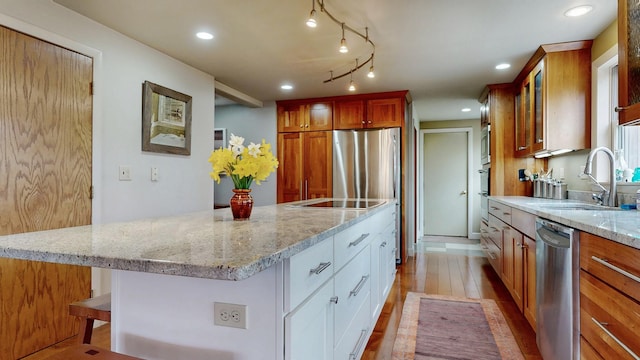 kitchen with appliances with stainless steel finishes, wood finished floors, a sink, light stone counters, and glass insert cabinets