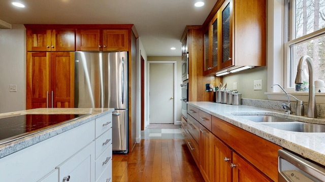 kitchen with light stone countertops, a sink, stainless steel appliances, recessed lighting, and glass insert cabinets