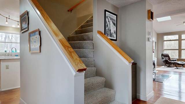 stairway featuring baseboards, ceiling fan, track lighting, and wood finished floors
