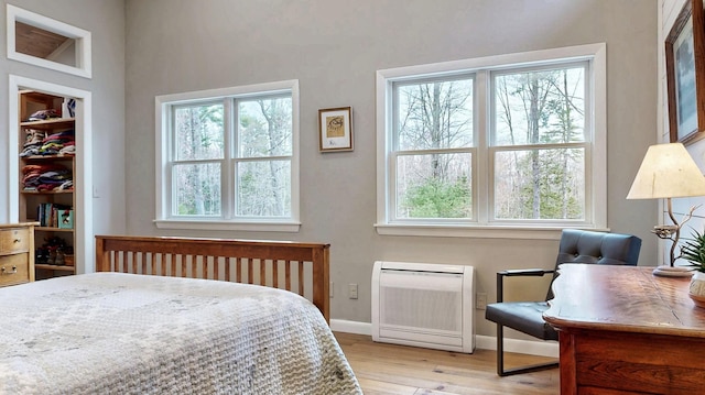 bedroom with baseboards, heating unit, wood finished floors, and multiple windows