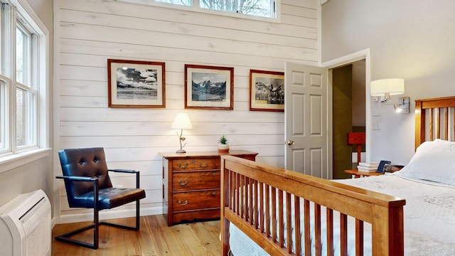 bedroom with wooden walls, a wall mounted air conditioner, and light wood-style flooring
