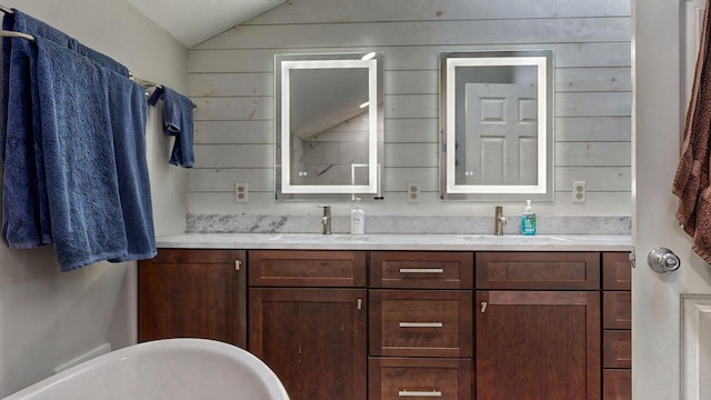 full bath with double vanity, a sink, a freestanding tub, and lofted ceiling