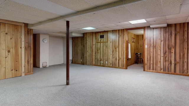 finished below grade area featuring carpet flooring, wooden walls, visible vents, and a drop ceiling