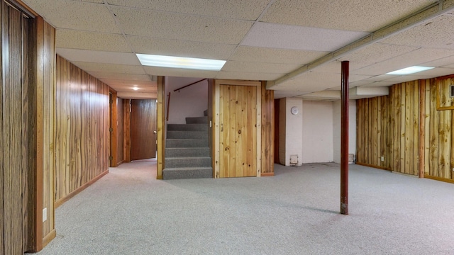 finished below grade area featuring carpet floors, wood walls, a drop ceiling, and stairway