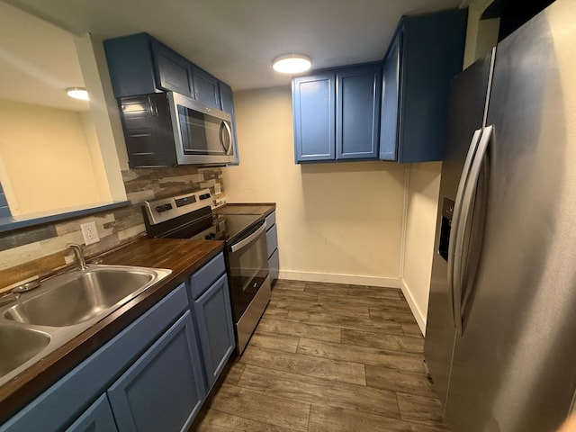 kitchen featuring baseboards, dark wood-type flooring, stainless steel appliances, backsplash, and blue cabinetry