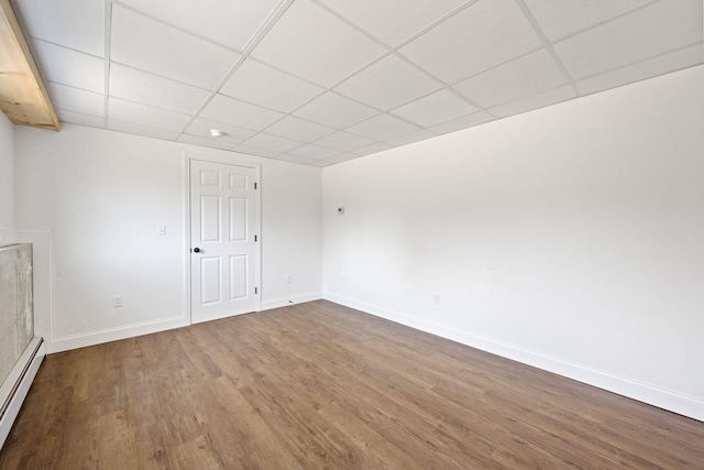 empty room featuring wood finished floors, baseboards, a paneled ceiling, and a baseboard heating unit
