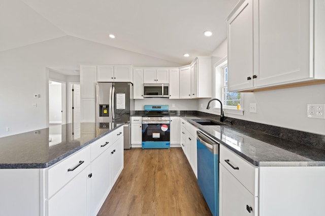 kitchen with white cabinets, stainless steel appliances, a sink, and lofted ceiling