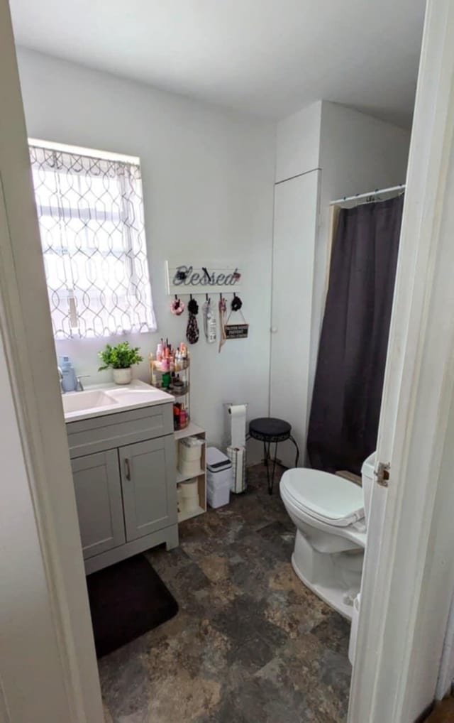 full bathroom featuring vanity, stone finish floor, toilet, and curtained shower