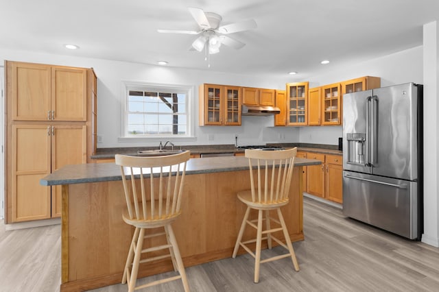 kitchen with a kitchen bar, dark countertops, light wood-type flooring, high end refrigerator, and under cabinet range hood