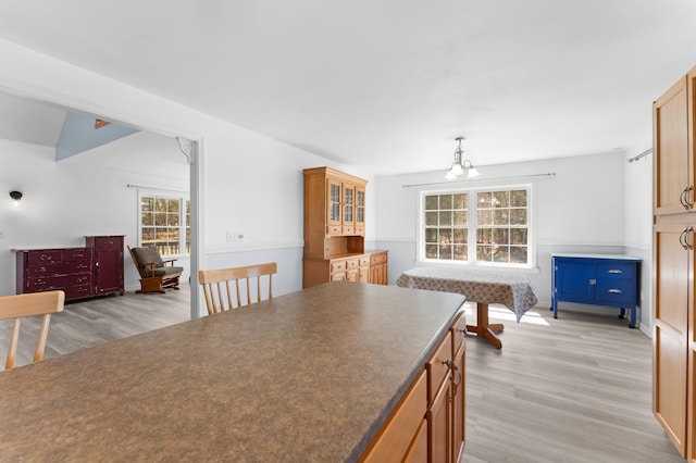 kitchen featuring light wood-style flooring, hanging light fixtures, dark countertops, and glass insert cabinets