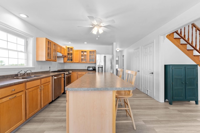 kitchen with ceiling fan, a sink, a breakfast bar area, stainless steel appliances, and under cabinet range hood