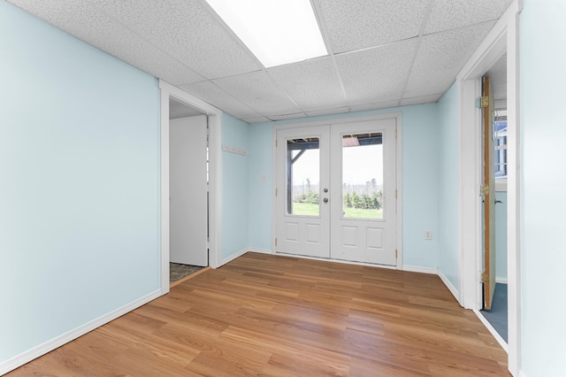 interior space featuring french doors, baseboards, light wood finished floors, and a drop ceiling