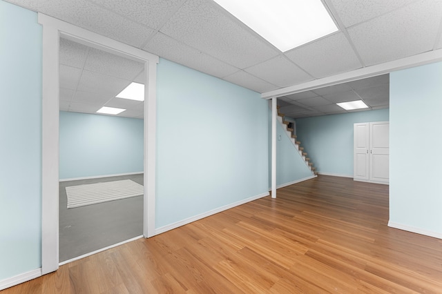 finished below grade area featuring baseboards, a drop ceiling, stairs, and wood finished floors