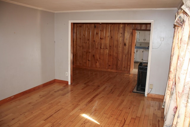 empty room with baseboards, light wood finished floors, and crown molding